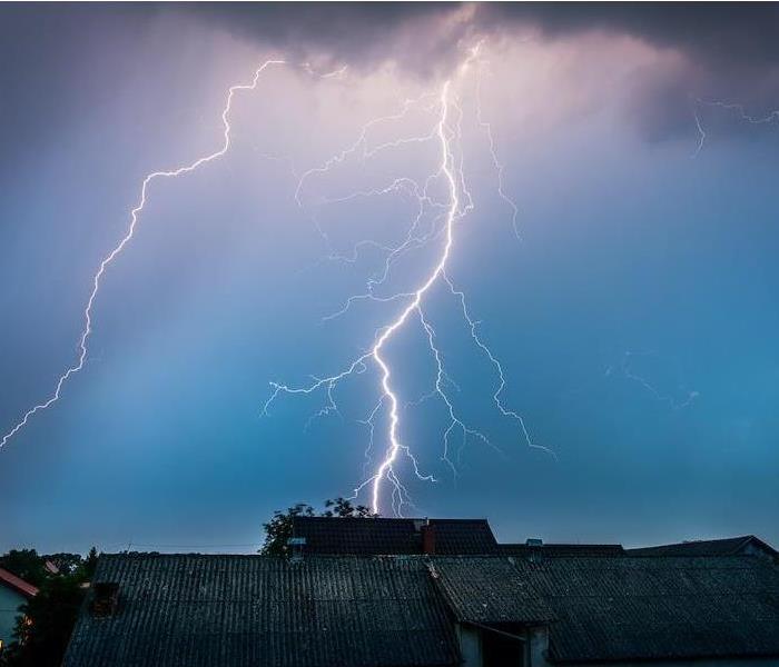 ?Lightning in purple, blue, and gray sky over houses.